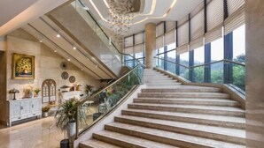 Un'imponente scalinata con ringhiera in vetro che conduce a un soffitto alto illuminato da un moderno lampadario.