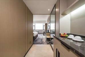 A hotel room with a bed, a desk, a chair, a small table, and a fruit bowl on the counter. - Minzhong Grand Hotel (Youxi)