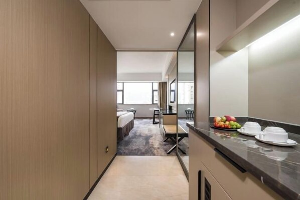 A hotel room with a bed, a desk, a chair, a small table, and a fruit bowl on the counter. - Minzhong Grand Hotel (Youxi)