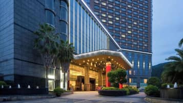 A modern hotel entrance with a curved facade, a well-lit entrance area, and a landscaped garden.