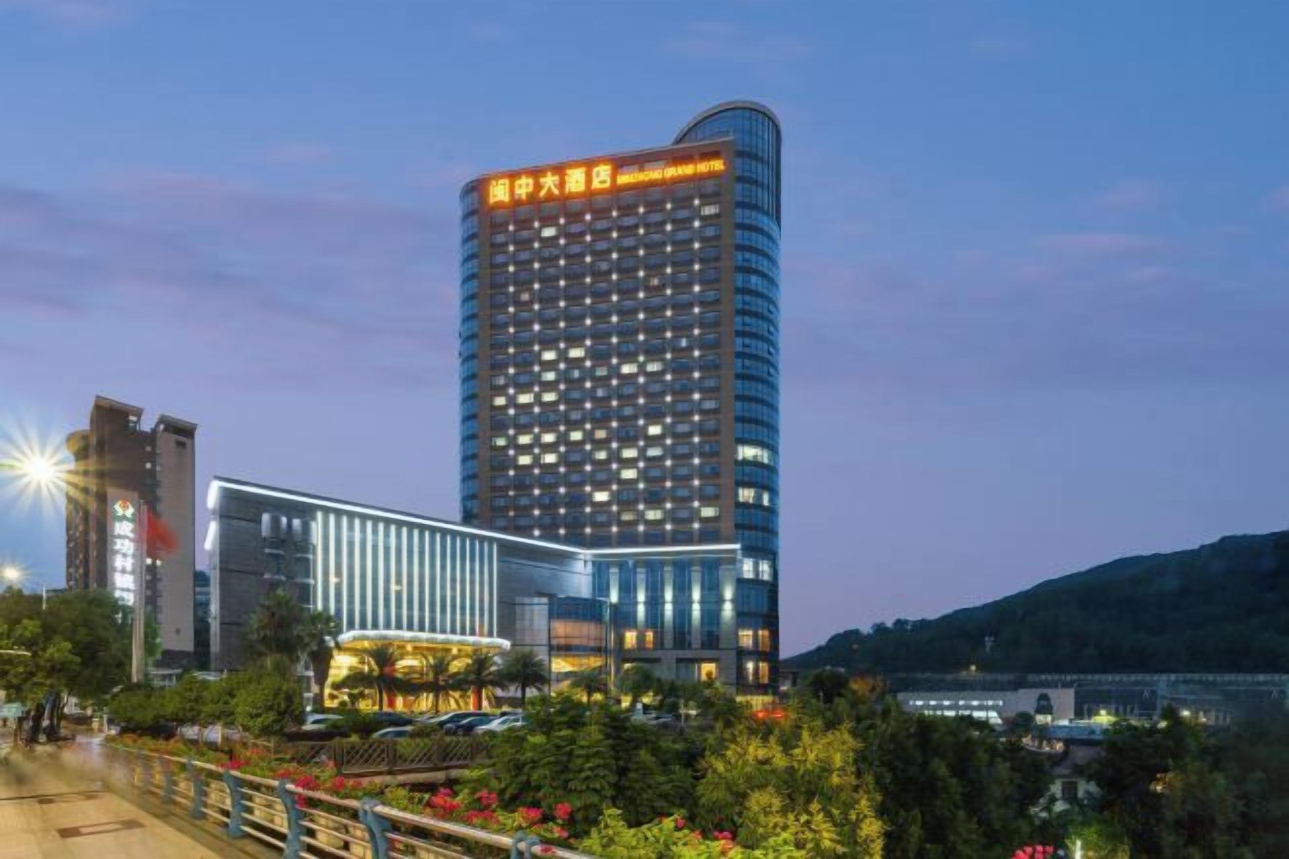 A high-rise hotel with a modern facade, situated by a waterfront with a bridge in the foreground.