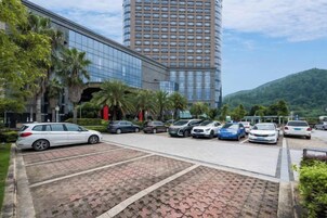Um estacionamento com vários carros, um edifício moderno com fachada de vidro e uma montanha ao fundo.