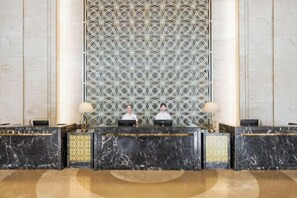 A reception area with a marble reception desk, two receptionists, and a patterned wall behind them. - Minzhong Grand Hotel (Youxi)