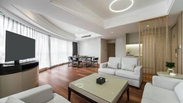 A modern living room with a flat-screen TV, a sofa, a coffee table, and a dining area with a table and chairs.