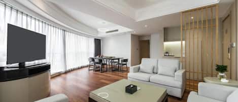 A modern living room with a flat-screen TV, a sofa, a coffee table, and a dining area with a table and chairs.