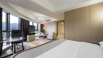 A modern hotel room with a large bed, a desk with a chair, a sofa, and a TV.