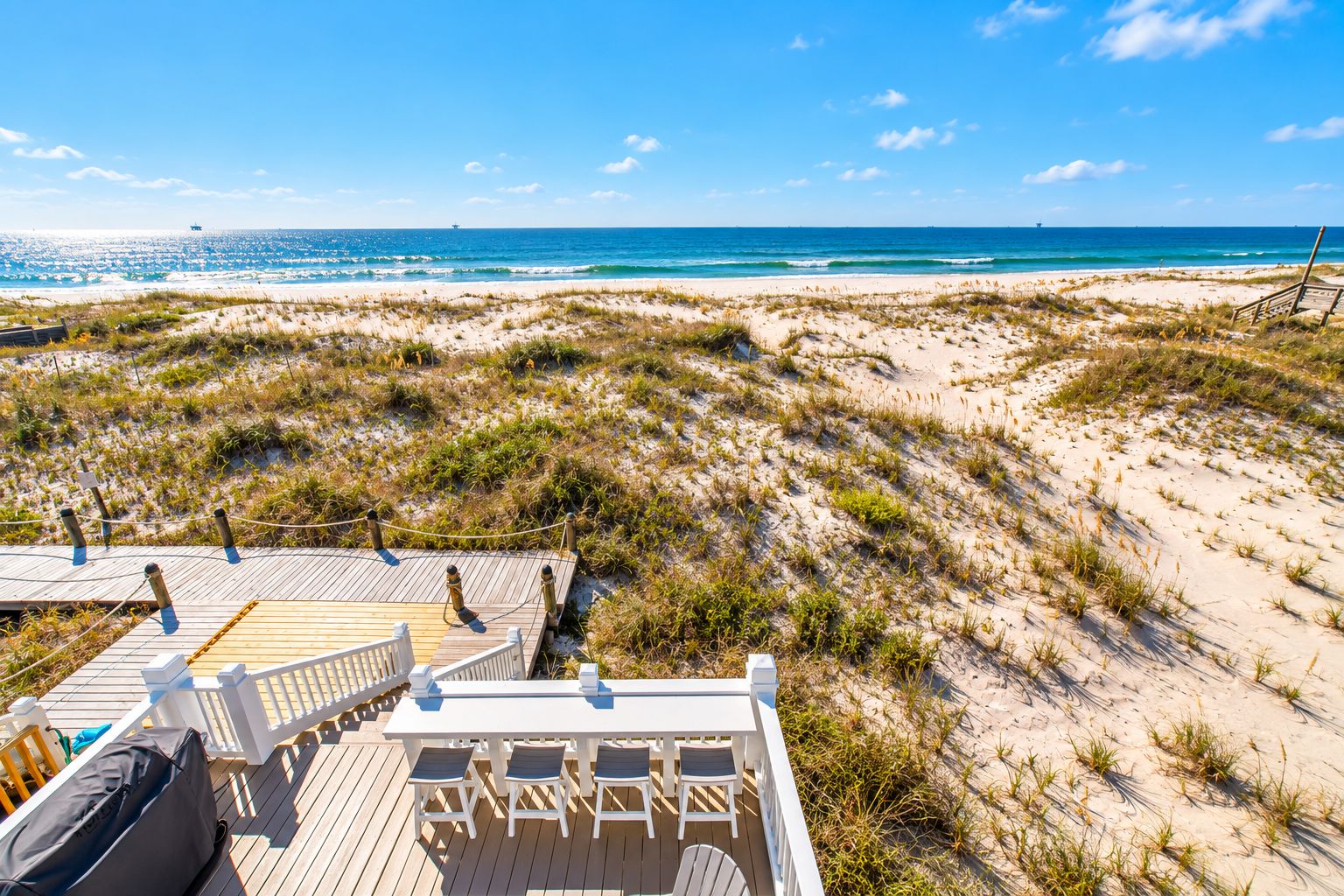 From the deck, the dune boardwalk leads toward the white-sand shoreline while bar seating overlooks the Gulf.