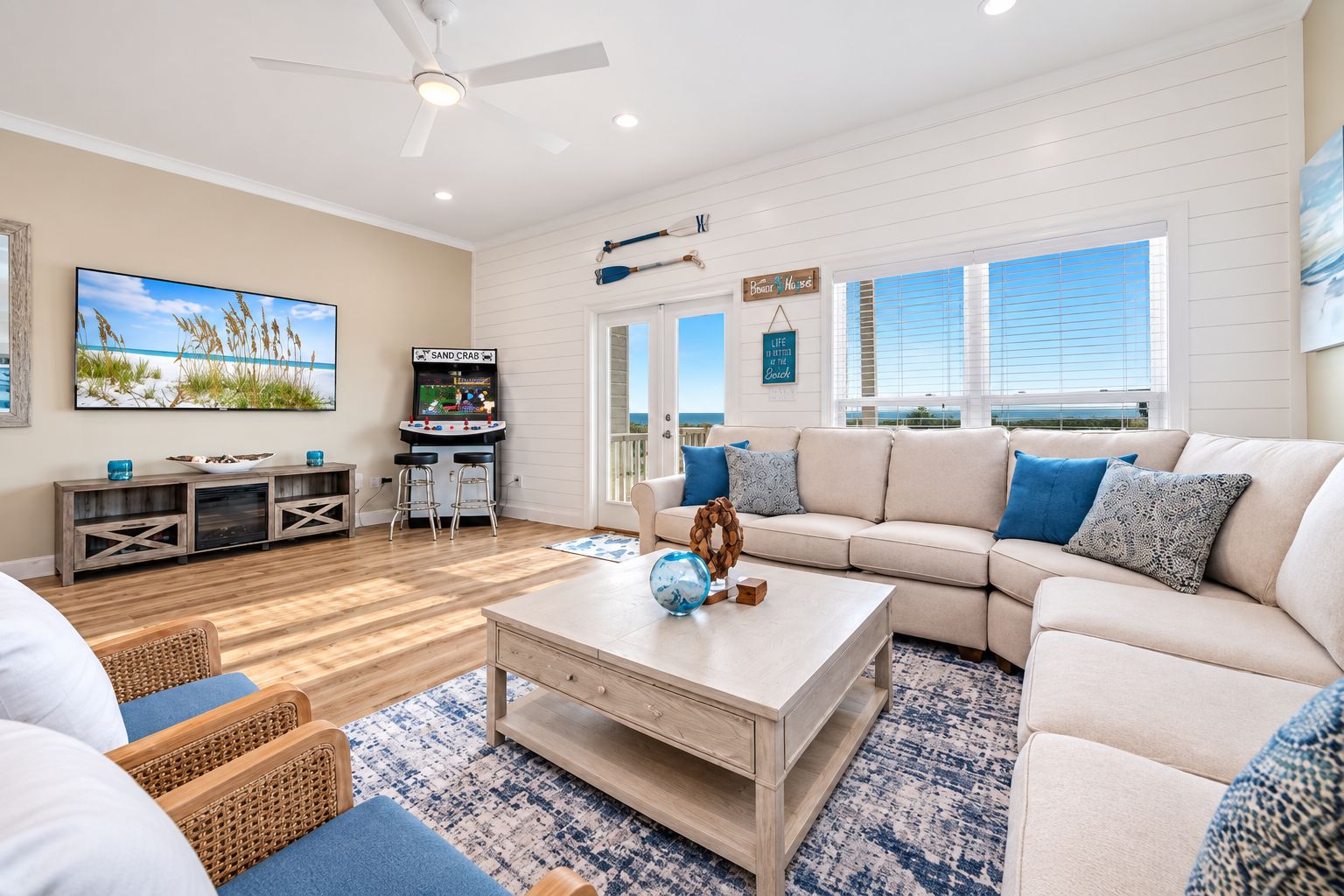 A spacious living room with a large window, a ceiling fan, a television, and a sand crab arcade game.