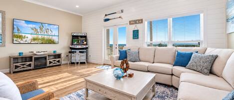 A spacious living room with a large window, a ceiling fan, a television, and a sand crab arcade game.