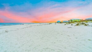 Ein Strand mit blauem Himmel und Sonnenuntergang. Im Hintergrund sind Gebäude zu sehen.