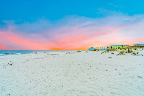 A beach with a clear sky and a sunset. There are buildings in the background. - Oceanfront Home · Pool · Arcade & Fire Pit (Gulf Shores)