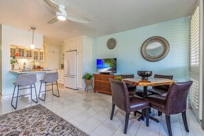 Una cocina moderna con armarios blancos, un comedor con mesa de madera y sillas de cuero, y un televisor montado en la pared.