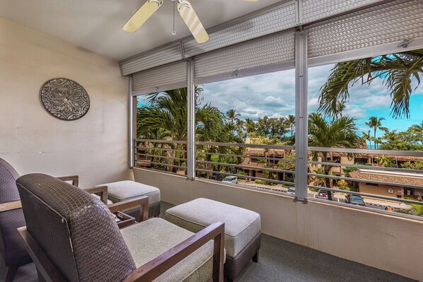 Un balcón con vistas a palmeras y edificios, un ventilador de techo y una silla de mimbre.