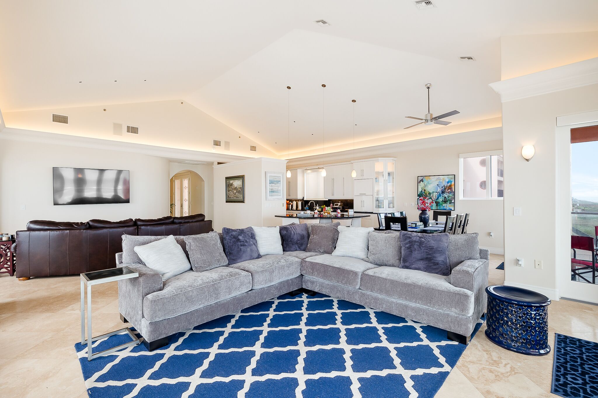 A modern living room with a gray sectional sofa, a blue patterned rug, and a ceiling fan.