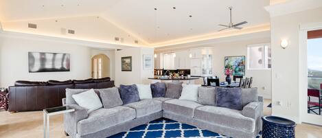 A modern living room with a gray sectional sofa, a blue patterned rug, and a ceiling fan.