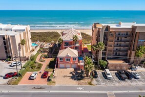 Un hôtel situé en bord de mer, avec un bâtiment à toit rouge, un parking et une vue sur l’océan.