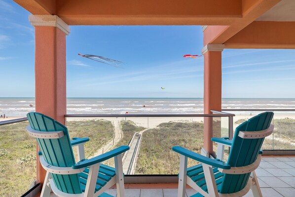 Un balcon avec deux fauteuils Adirondack verts donnant sur une plage.