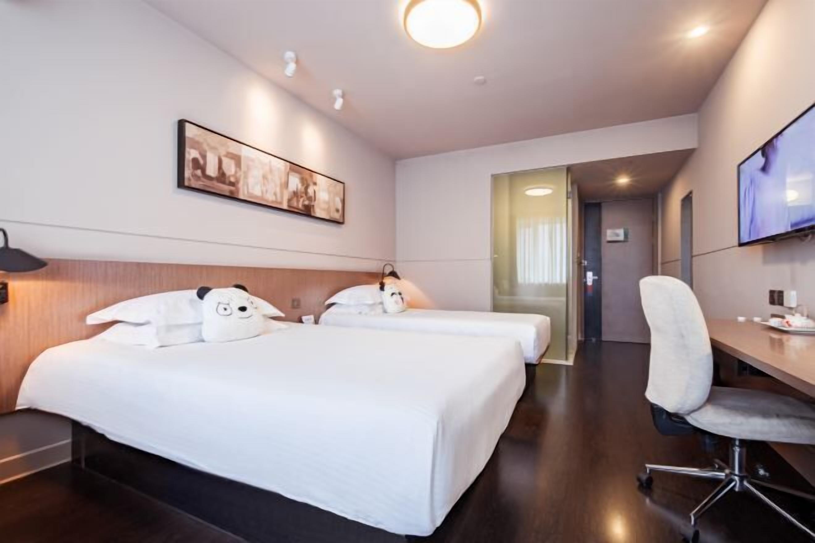 Une chambre d’hôtel avec deux lits, un bureau, une chaise, une télévision et un tableau encadré au mur.