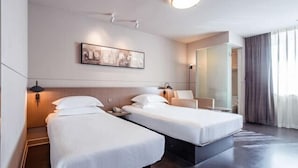 A modern hotel room with two beds, a large mirror, and a painting on the wall.