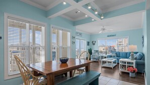 A spacious living area with a wooden dining table, blue sofa, and white side tables. - CottageVacations4u "Shore Thing"- ocean views-direct beach access-pool club<br>Golf cart friendly (Ocean Isle Beach)