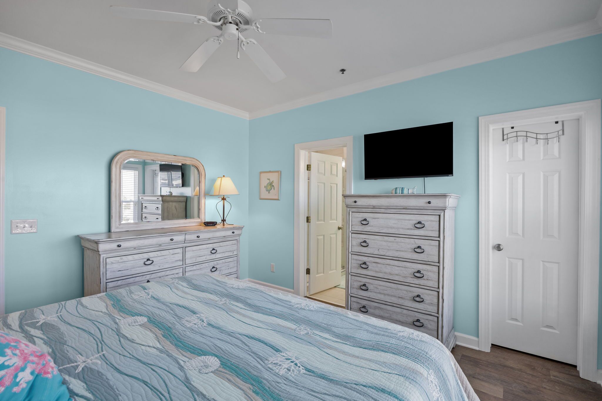 Une chambre à coucher comprenant un lit, une commode, un miroir, une lampe, un téléviseur et une porte.