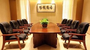 Un salón de conferencias con una amplia mesa de madera rodeada de sillas de cuero, una planta en maceta sobre la mesa y un cartel enmarcado en la pared.