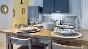 A modern kitchen with a dining table set for two, featuring a bowl, plates, and wine glasses.