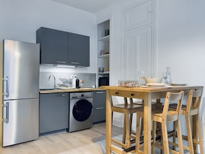 A modern kitchen with stainless steel appliances, a wooden dining table, and bar stools.