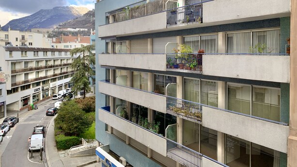 A multi-story building with balconies, a street view, and a mountain in the background.