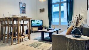 A modern living room with a dining area, a flat-screen TV, and a large window with curtains.