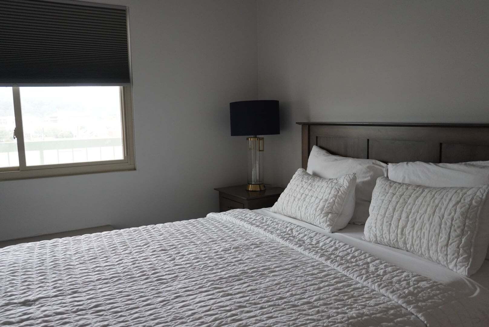 Une chambre à coucher avec un grand lit, une table de chevet avec une lampe et une fenêtre avec des stores.