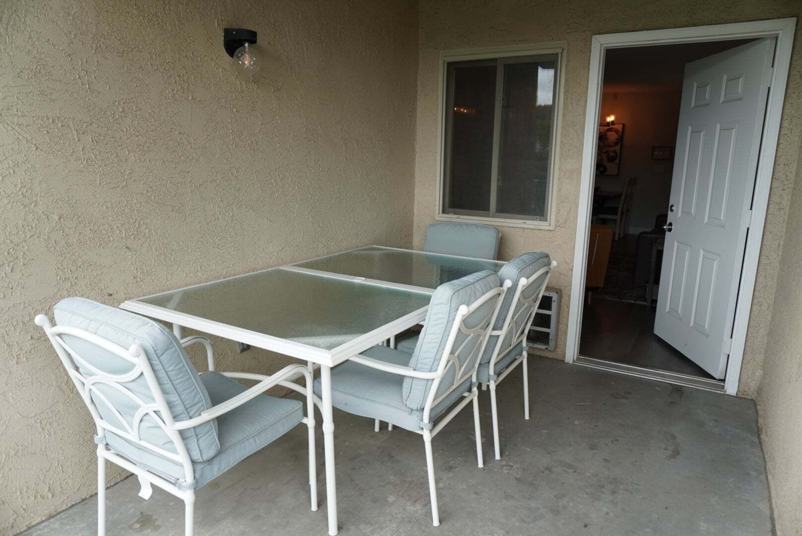 A glass-top table with four chairs, a window, and a door leading to an interior space.