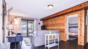 Ett mysigt rum med ett träpanelat tak, en soffa, ett litet bord med en lampa och utsikt genom en glasdörr.