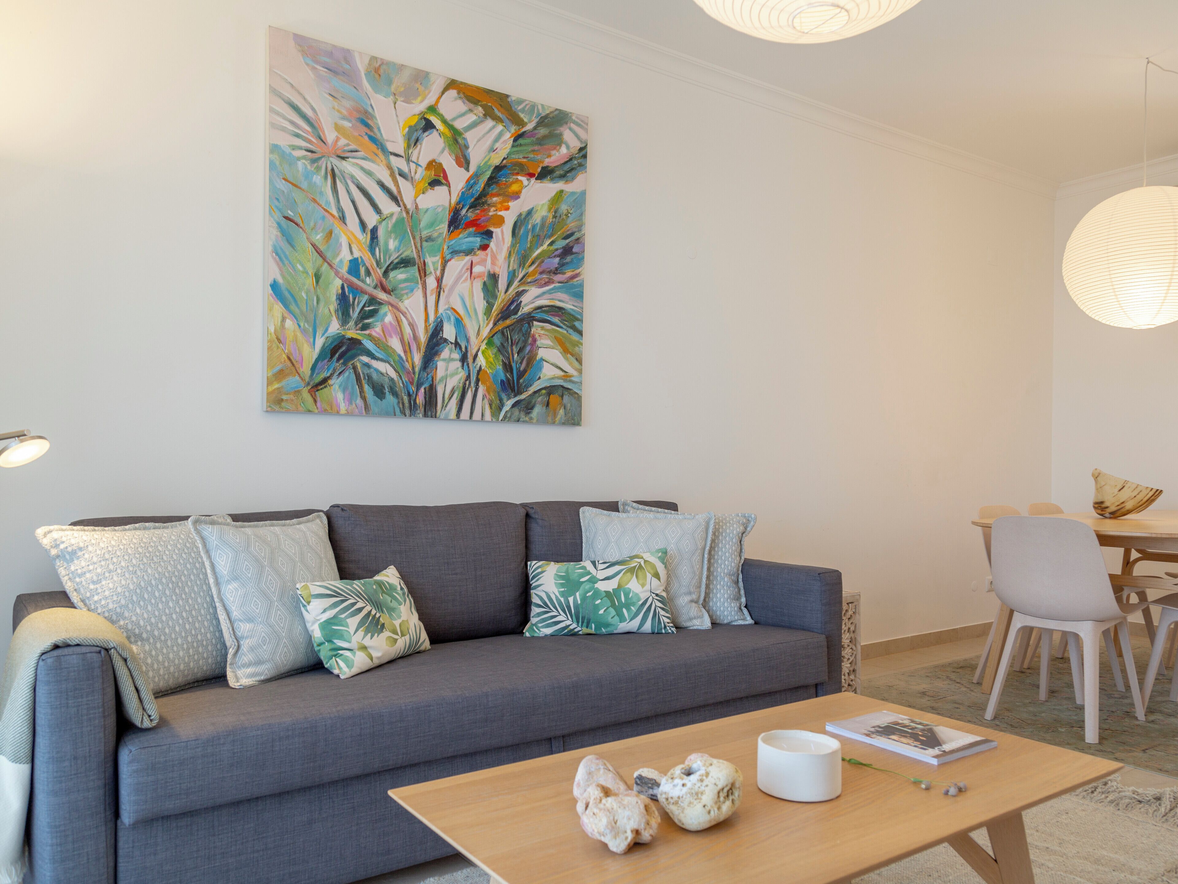 Ein modernes Wohnzimmer mit grauem Sofa, gemusterten Kissen, einem Holztisch und einem großen abstrakten Gemälde an der Wand.