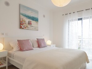 Un dormitorio con una cama, dos mesitas de noche, un cuadro en la pared y una ventana con cortinas.