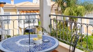 Ein runder Tisch mit Stühlen auf einem Balkon, eine Weinflasche und ein Glas darauf.