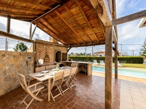 An outdoor patio with a brick oven, wooden furniture, and a pool.