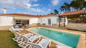 A pool area with white lounge chairs, a stone wall, and a covered patio.