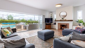 A spacious living area with a large TV, comfortable seating, a fireplace, and a view of a swimming pool.