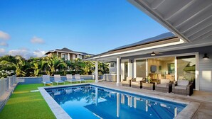 Un área de piscina moderna con una piscina azul cristalina, rodeada de césped artificial y sillas de descanso blancas.