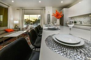 A modern dining area with a long table set for four, a sofa, and a view of the outdoors.