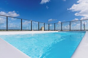 A swimming pool with clear blue water, surrounded by a glass fence, and a clear sky with clouds in the background. - Stylish 2BR Condo w/ Pool near Palm Beach (Noord)