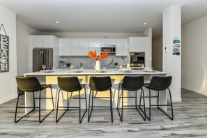 A modern kitchen with white cabinets, a central island with bar stools, and a decorative vase with orange flowers.