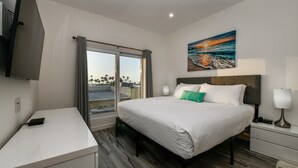 Una camera d'albergo con un letto, comodini, una scrivania, una televisione e un quadro raffigurante una spiaggia.