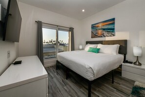 A hotel room with a bed, bedside tables, a desk, a TV, and a painting of a beach scene. - Prime Aruba Location: 2BR Condo near Palm Beach (Noord)
