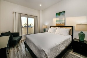 Ein Hotelzimmer mit einem großen Bett, einem Schreibtisch, einem Sessel, einem Fenster mit Vorhängen und Blick auf den Strand.
