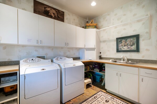 A laundry room with two front-loading washing machines, a small stool, and a shelf with various items.