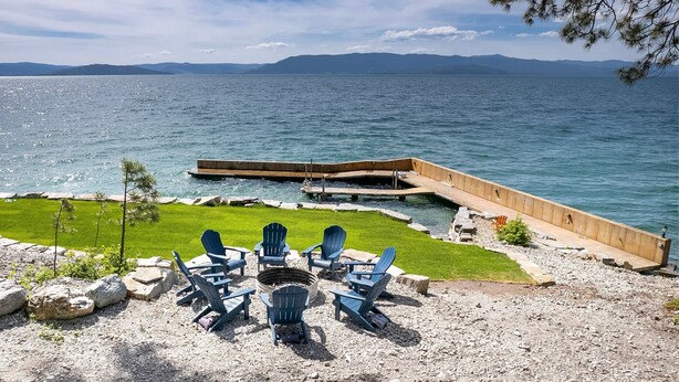 Une terrasse au bord du lac, avec des fauteuils Adirondack, un foyer et une jetée en bois qui s’avance dans l’eau.