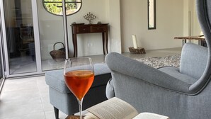 A modern living room with a glass door leading to a balcony, a grey sofa, a small wooden table with a book and a glass of drink, and a floor lamp. - Modern architect's house in olive grove with sea views (Vasia)
