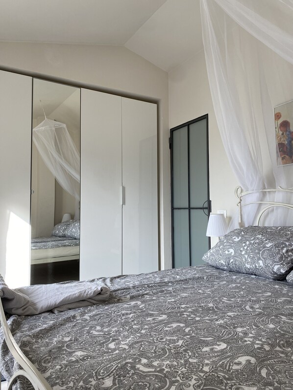 Un dormitorio con cama, armario y ventana con cortinas traslúcidas.